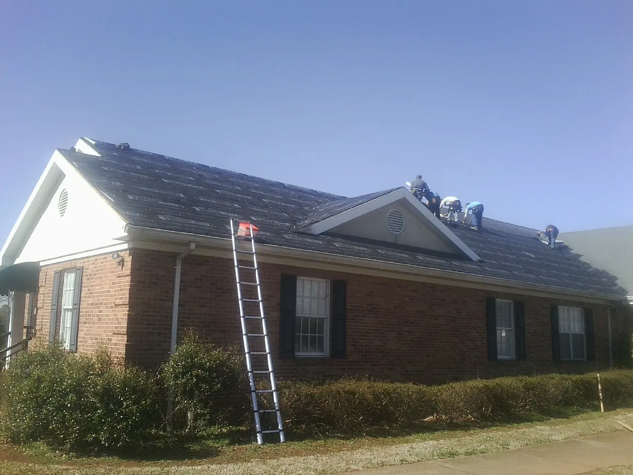 Crew tearing shingles off a brick ranch roof with a ladder set — Emergency Roof Repair work by our crew in Suffern