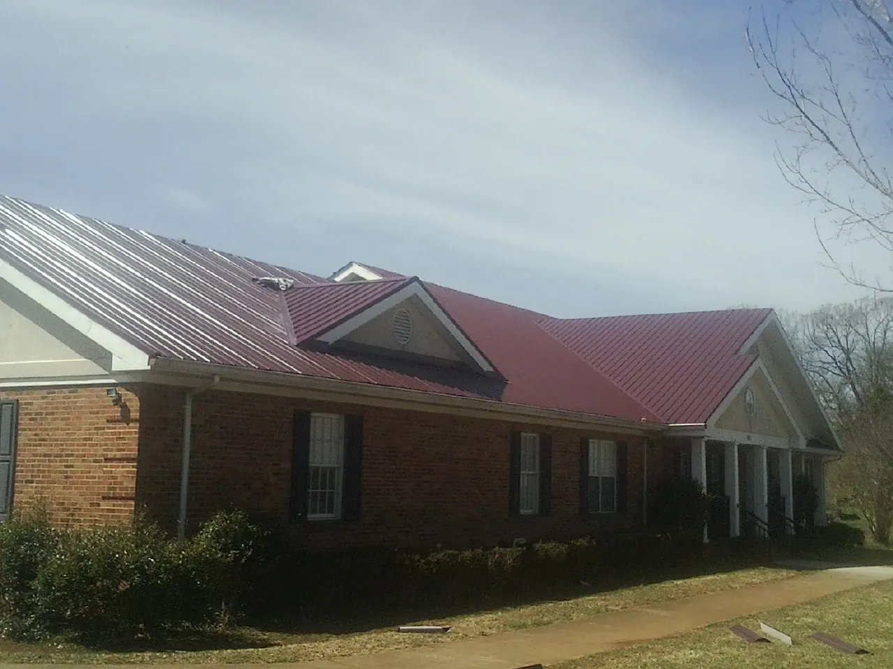 Red metal roof with gabled entries on a long brick building, from a Hail Damage Roof Repair job in Suffern