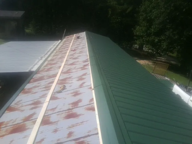 Old rusted panels beside newly installed green metal roofing — Wind Damage Roof Repair by Roofing Brothers in Suffern
