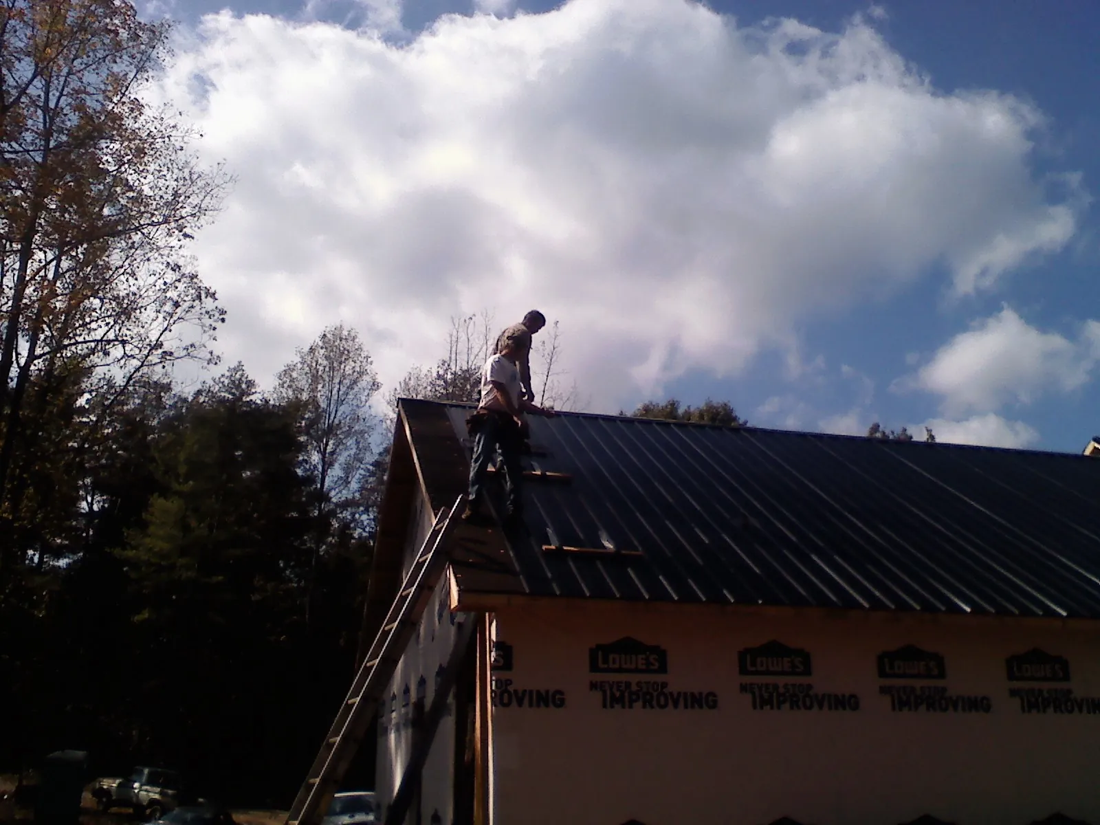 Roofer fastening dark metal panels high against a cloudy sky, from a Roof Inspection job in Suffern