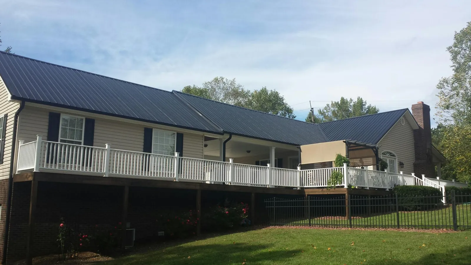 Black metal roof above a long white railed deck on a hillside home in Suffern