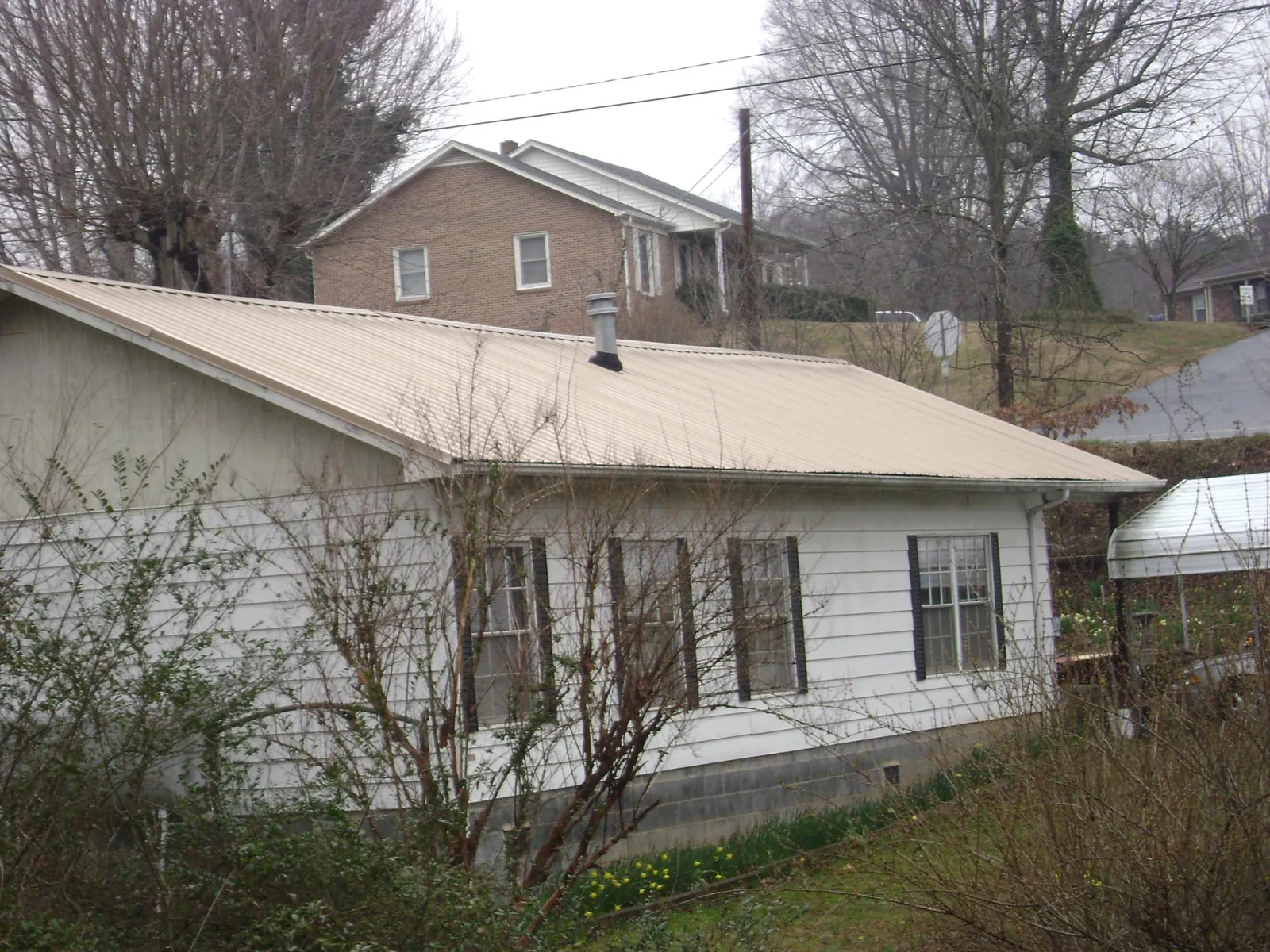 Tan metal roof on a white sided house set into a hillside — Commercial Roofing by Roofing Brothers in Suffern